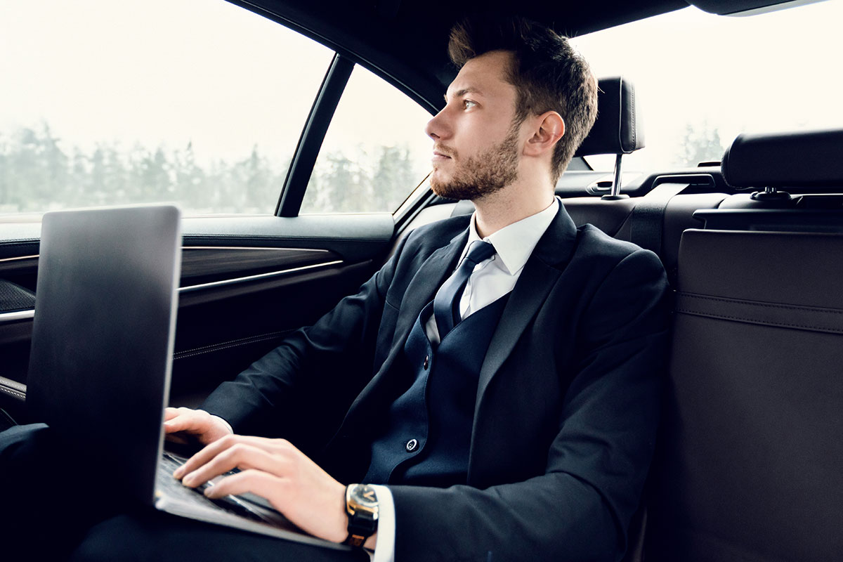 Employee working on laptop in chauffeur-driven car - The future of corporate travel and employee transportation.